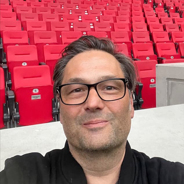 Porträt von Michael Weiß mit Brille vor roten Sitzreihen